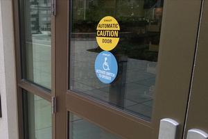 An automatic door on campus. Stickers on the door read, 'Automatic Door, Caution,' and 'Activate Switch to Operate.'