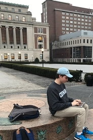 A young man sits outdoors with a laptop