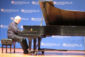A white-haired man plays the piano onstage