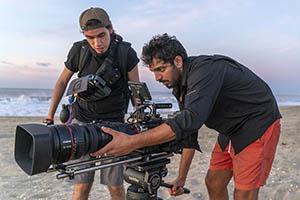 Emiliano Ruprah and crew member filming on a beach