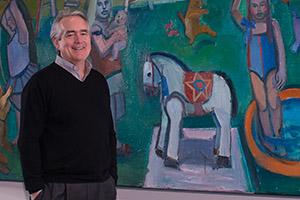 Jack Rasmussen stands smiling in front of a painting in the AU Museum.