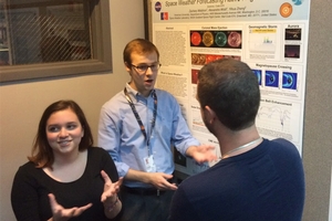 Alexandra Wold and Zach Waldron stand by a poster gesturing