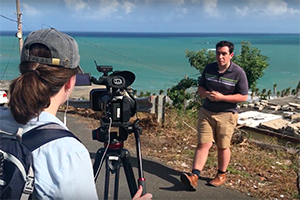 Two students film for their journalism class in front of the ocean in Puerto Rico