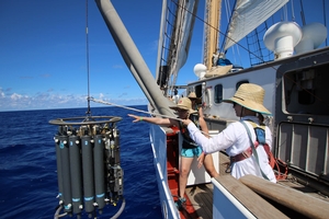 Two people lower an object from the side of a boat