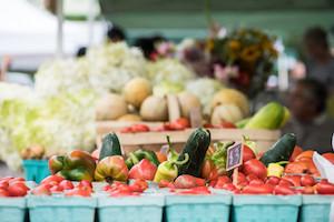 Cardboard containers of tomatoes, squash, and peppers at a farmer's market.